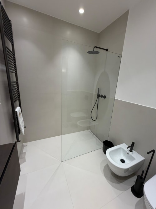 Modern bathroom at Maisons Milano with walk-in shower, white sink, black fixtures, heated towel rack, and recessed lighting