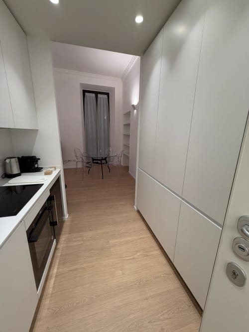Corridoio di cucina moderna nell'appartamento Maisons Milano con mobili bianchi, pavimento in legno e vista sulla zona pranzo in vetro