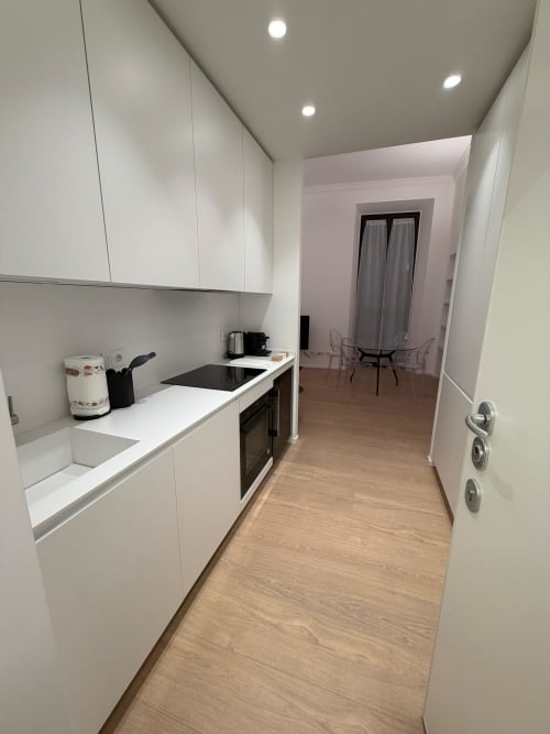 Cucina bianca moderna con stufa nera nell'appartamento Maisons Milano, pavimenti in legno, che conduce al soggiorno