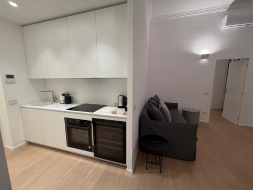 Monolocale moderno a Maisons Milano con cucina bianca open-plan, elettrodomestici neri e divano scuro in soggiorno