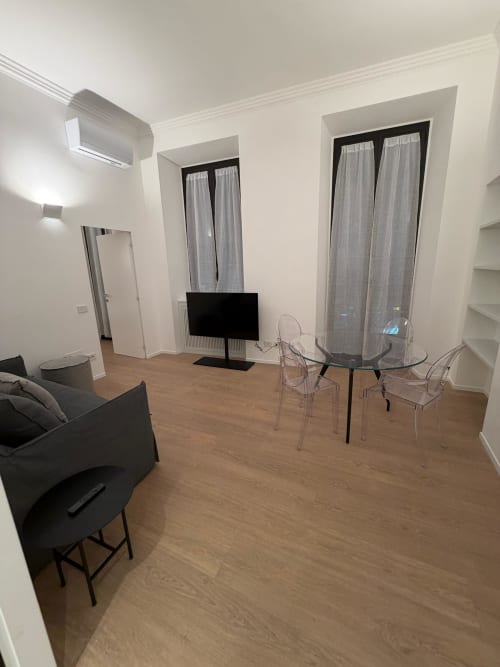 Moderno appartamento a Milano con pavimenti in legno, TV, tavolo da pranzo in vetro, sedie trasparenti e finestre panoramiche