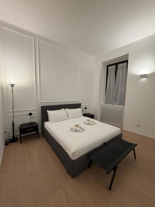 Camera moderna presso Maisons Milano con letto nero, biancheria bianca, pavimenti in legno e arredamento minimalista