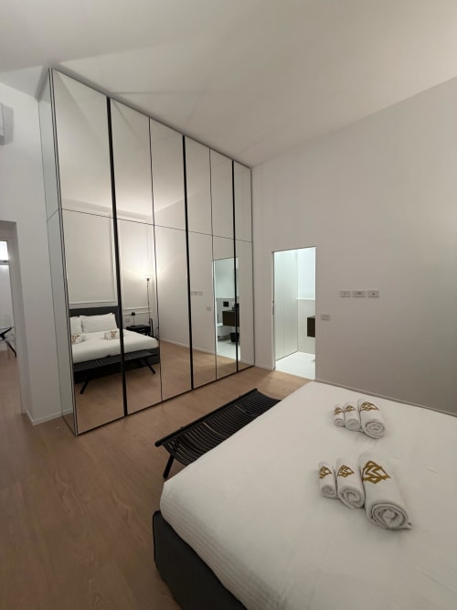 Camera moderna Maisons Milano con armadio a specchio, asciugamani arrotolati e pavimentazione in legno
