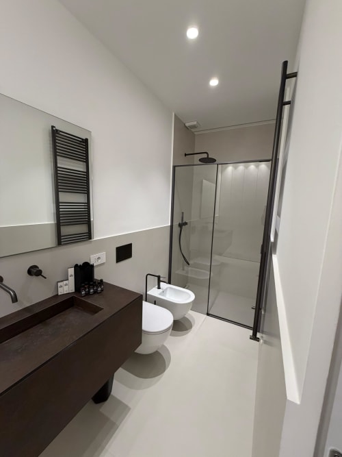 Bagno moderno di Maisons Milano con vanity scuro, wc bianco, bidet e doccia walk-in con rubinetteria nera
