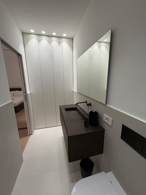 Bagno moderno presso Maisons Milano con vanity scuro, specchio illuminato, pareti bianche e elementi contemporanei in Via Dei