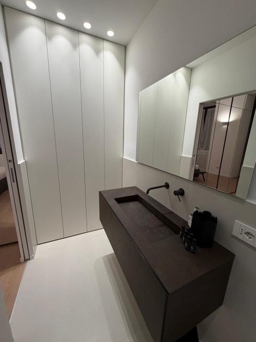 Bagno moderno a Maisons Milano con lavabo scuro, parete a specchio, pannellatura bianca e illuminazione incassata