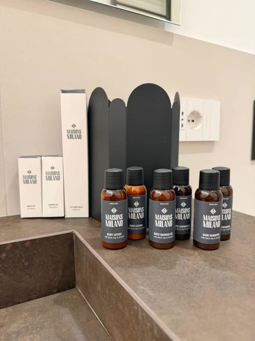 Espositore di amenities lusso Maisons Milano con confezioni nere e bottiglie ambrate sul bancone del bagno