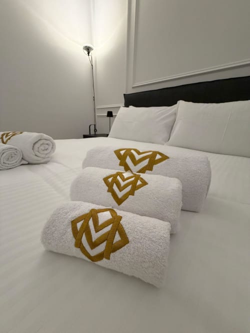 Camera da letto Maisons Milano con asciugamani bianchi a motivi geometrici dorati disposti su letto bianco con testiera nera