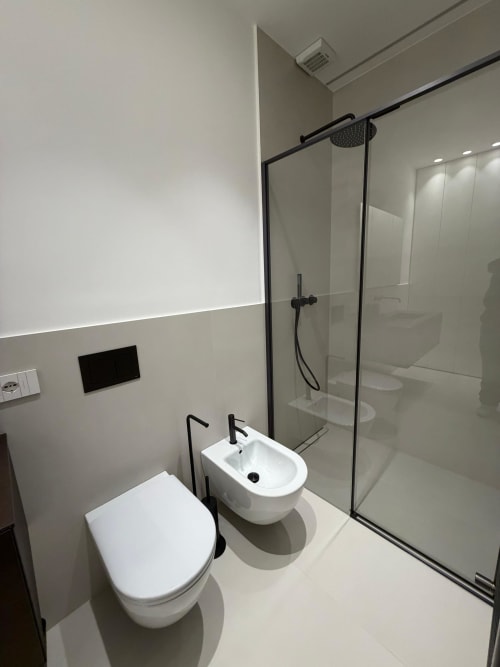 Bagno moderno di Maisons Milano con toilette bianca, bidet e doccia walk-in con accessori neri