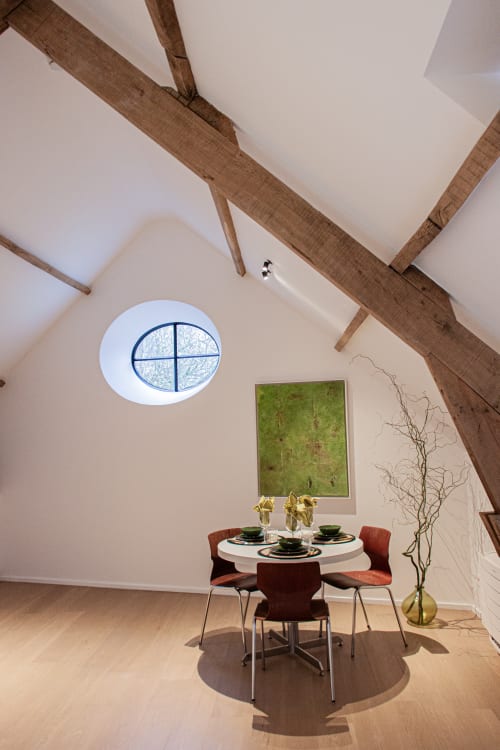 Modern dining area in Studio Catherine at Castanea Business & Suites with round table, red chairs, oval window, and exposed