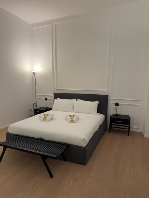 Modern bedroom at Maisons Milano with black bed, white linens, nightstands, and minimalist decor