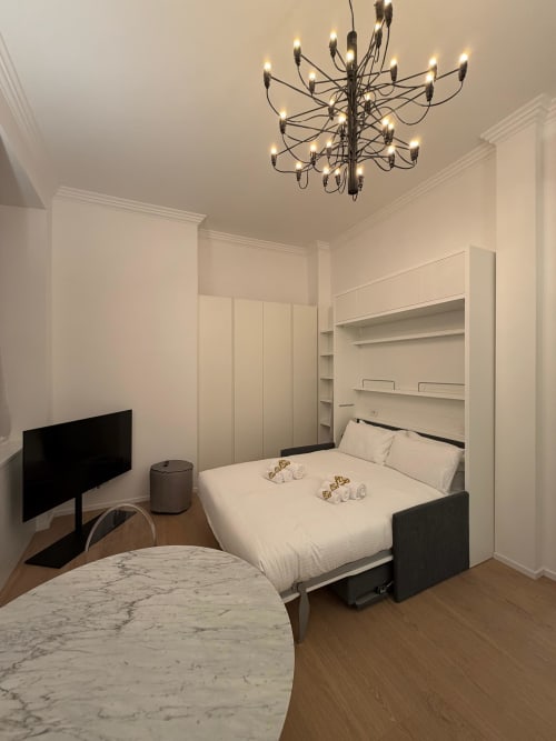 Modern hotel room at Maisons Milano with twin beds, elegant chandelier, built-in shelving, and marble accent table