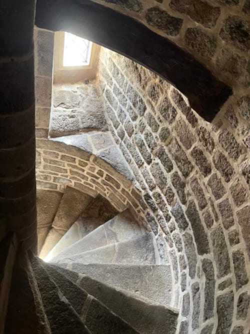 Escalier en pierre avec fenêtre en arc du Manoir de Fornebello, Châtelaudren-Plouagat, offrant une vue sur le jardin depuis la Chambre