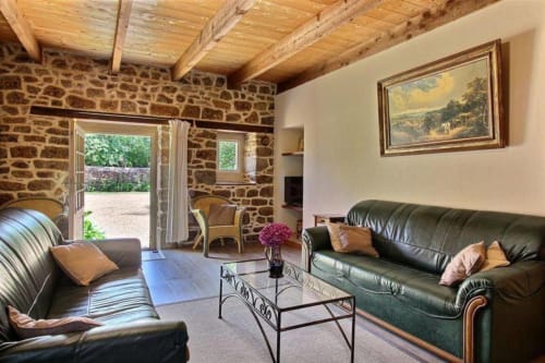 Élégant salon de villa en pierre aux poutres apparentes, canapés en cuir vert et vue sur les jardins du Manoir de Fornebello