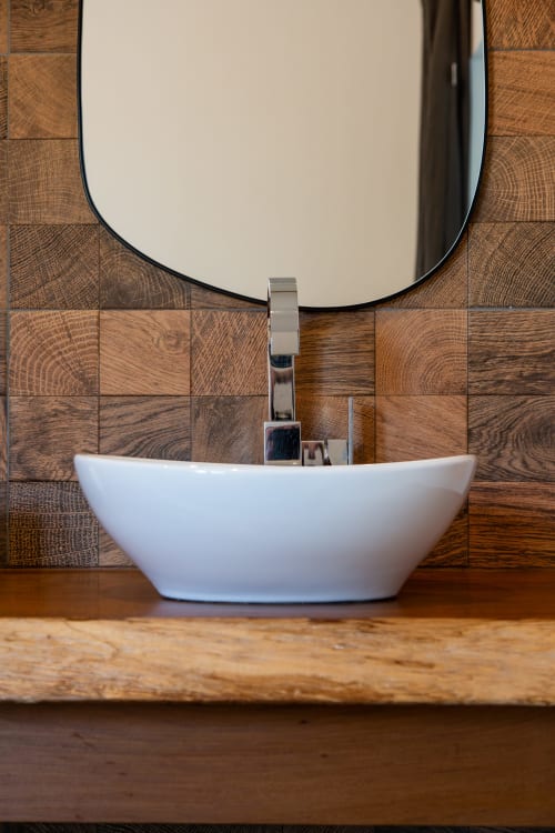 Modern white oval sink with chrome faucet on wooden vanity, wood tile backsplash and round mirror at Villa Figue Blanche