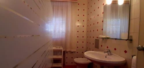 Bright bathroom in Rosa Suite at Belvedere del Lago, Montefiascone, with dual sinks, red tile accents, and windows with lake