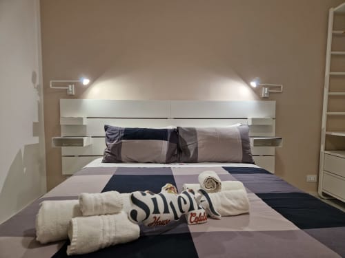 Camera da letto moderna a Sikelia House Cefalù con testata bianca, illuminazione d'atmosfera, biancheria grigia e asciugamani arrotolati