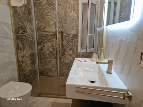 Bagno moderno di Sikelia House Cefalù con finiture in marmo, doccia a pioggia e porte in vetro con motivi di palme.
