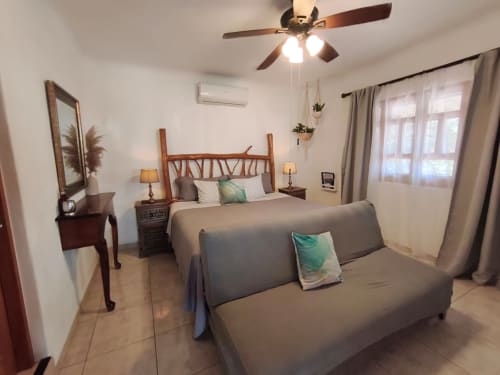 Dormitorio luminoso en Casa Punta Perula con cama de madera, sofá, ventilador de techo y vistas al océano