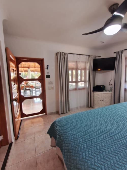 Dormitorio principal con ropa de cama turquesa, ventilador de techo, puerta de madera y vista al océano en Casa Punta Perula Boutique Hotel en Punta