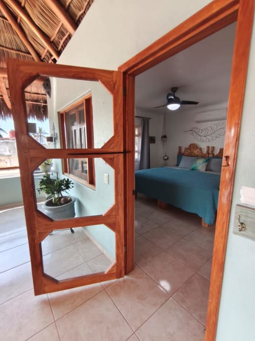 Puertas de cristal con marco de madera se abren al dormitorio Rey del Mar con cobertor color turquesa en Casa Punta Perula, Punta Perula México