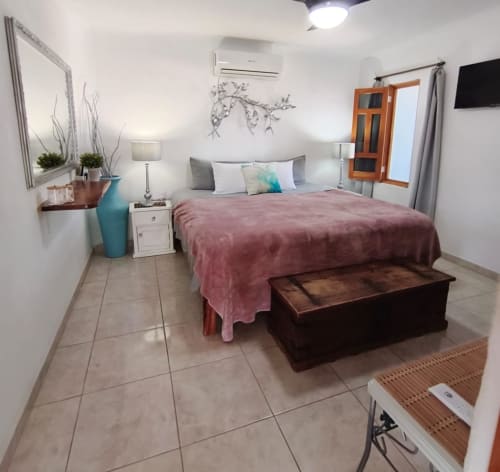 Moderna habitación en Casa Punta Perula con cama queen, manta rosa, banco de madera, espejo, florero turquesa y piso de azulejos