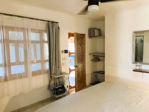 Dormitorio luminoso en Casa Punta Perula con cama, acceso a balcón, espejo, aire acondicionado y vistas al océano a través de cortinas translúcidas