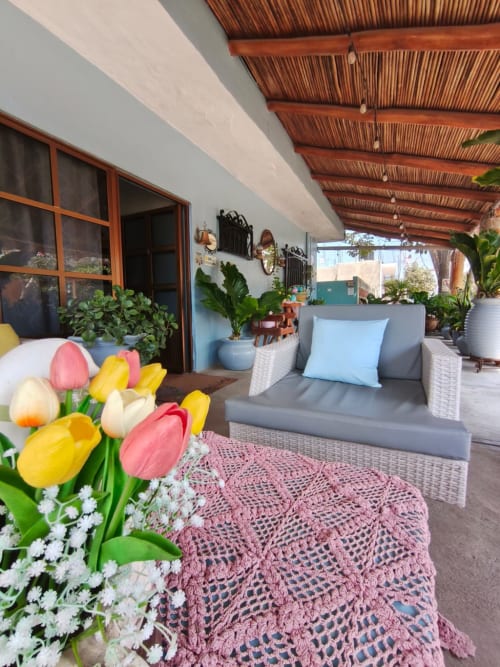 Terraza cubierta de Casa Punta Perula con muebles de mimbre, tulipanes coloridos, plantas en macetas y vistas al océano