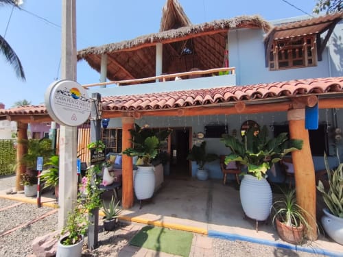 Entrada del Hotel Boutique Casa Punta Perula con techo de barro, macetas blancas y palapa de palma en Jalisco, México