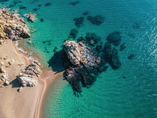 Aerial view of Calella's turquoise Mediterranean coastline with golden sandy beach and rocky outcrops