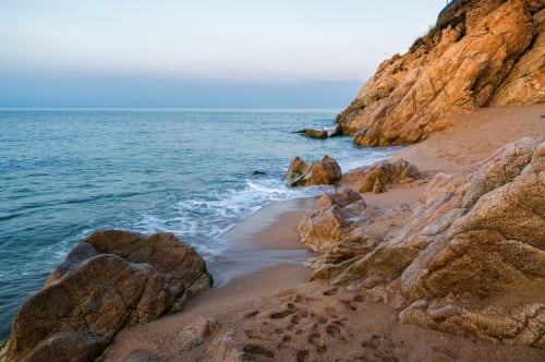 Cala rocosa al atardecer en Calella, España con acantilados dorados y aguas tranquilas del Mediterráneo