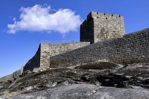 Muralhas e torre de fortaleza medieval em pedra com vista sobre Guarda, Portugal, sob céu azul limpo