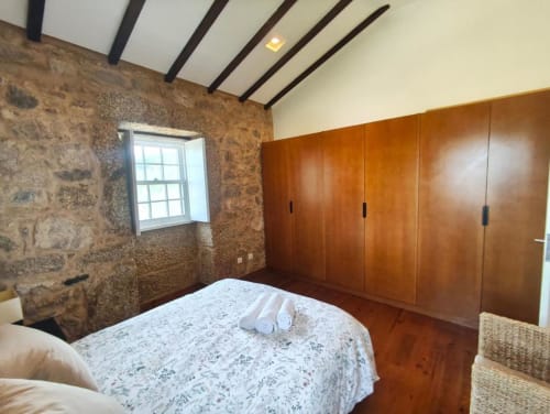 Quarto rústico em pedra na Coleção SM Stays, Guarda, com roupeiro em madeira e teto com vigas aparentes