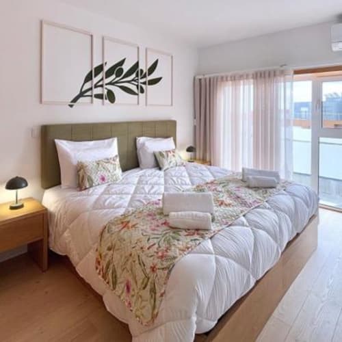 Quarto moderno na Coleção SM Stays em Guarda, PT, com cabeceira em tom oliva, roupa de cama floral e acesso à varanda.