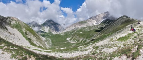 Valle alpina presso L'Aquila con prati verdi, picchi rocciosi e escursionisti negli Appennini