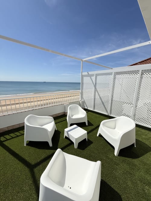 Terraza de playa moderna con muebles blancos, césped artificial y vistas al mar en Apartamentos A la Orilla del Mar,