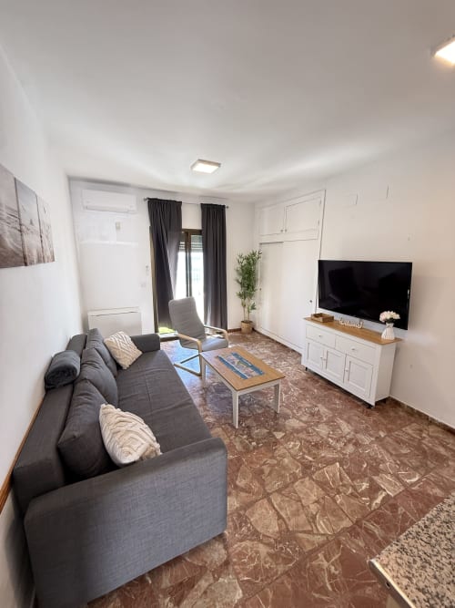 Moderna sala de estar con sofá gris, televisor y vistas al mar en Apartamentos A la Orilla del Mar, Matalascañas