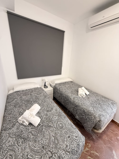 Dos camas gemelas con ropa de cama estampada y toallas blancas en luminoso dormitorio con TV en Apartamentos A la Orilla del Mar