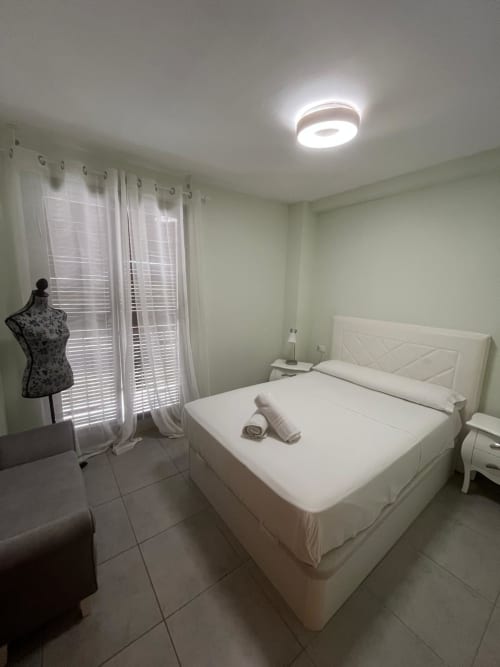 Chambre moderne de l'appartement Sant Jordi avec lit blanc, vue sur les montagnes et éclairage contemporain au plafond