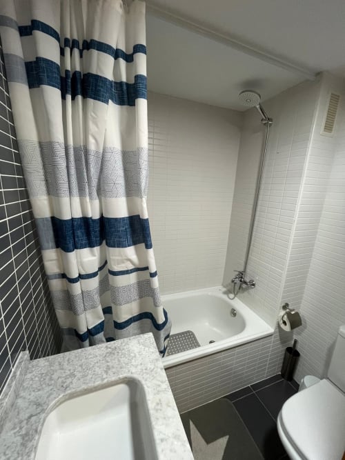 Salle de bains moderne avec rideau de douche bleu et blanc rayé, vanité en marbre, carrelage métro blanc et baignoire à Sant Jordi