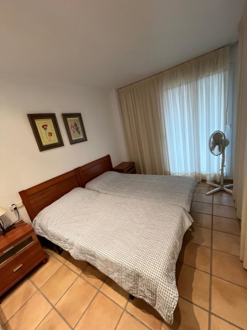 Chambre avec lit en bois, carrelage en terre cuite, rideaux beige et ventilateur dans l'appartement Sant Jordi avec vue sur le jardin