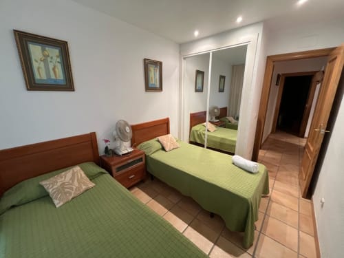 Deux lits jumeaux avec draps verts dans une chambre d'appartement Sant Jordi, armoire miroir et mobilier en bois