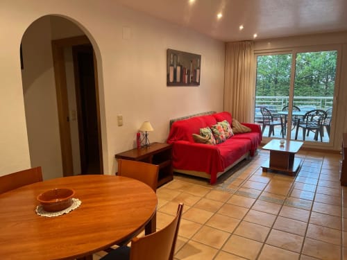 Lumineux séjour avec canapé rouge, salle à manger, carrelage terre cuite et balcon vue sur les jardins à Sant Jordi