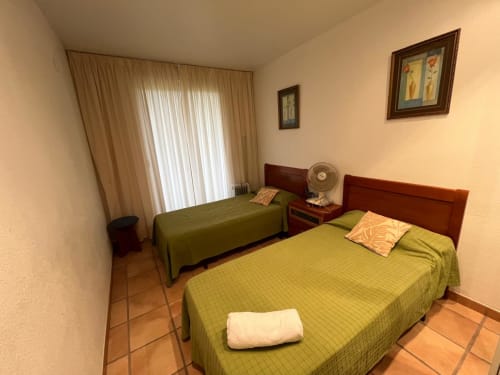 Deux lits jumeaux aux couvertures vertes dans une chambre lumineuse de l'appartement Sant Jordi avec vue sur la terrasse