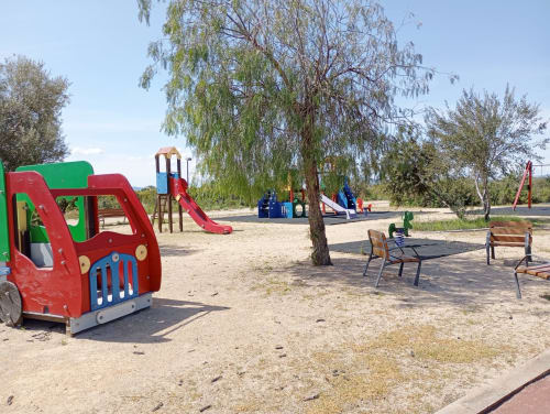 Aire de jeu avec équipements rouges et verts, grand saule et zone de détente dans le jardin de la propriété Sant Jordi.
