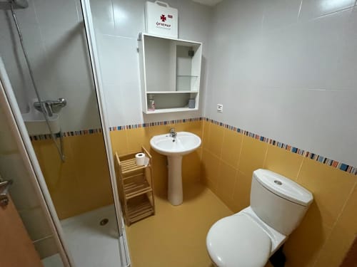 Salle de bain moderne aux carrelages dorés, lavabo sur colonne, toilettes, douche et rangements de l'appartement Golf Mar 4 chez Home Guardian