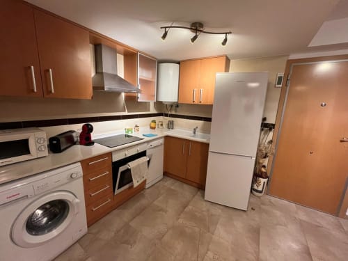 Cuisine moderne avec meubles en bois, électroménagers blancs et carrelage beige à l'appartement Residencia Golfmar, Sant Jordi