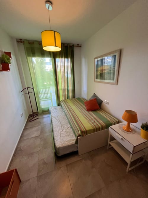 Chambre moderne de l'appartement Residencia Golfmar à Sant Jordi, avec literie rayée, vue sur jardin et mobilier contemporain
