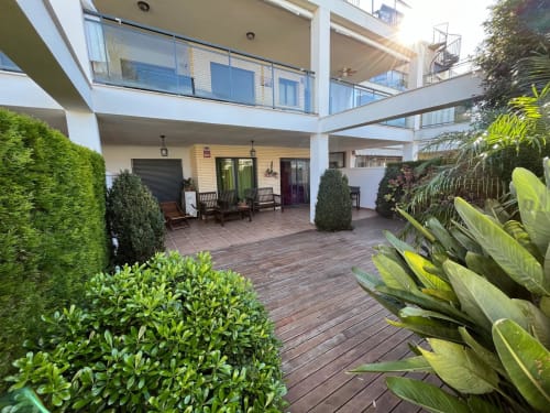 Terraza moderna en Residencia Golfmar con tarima de madera, exuberante vista al jardín, zona de descanso y barandales de cristal