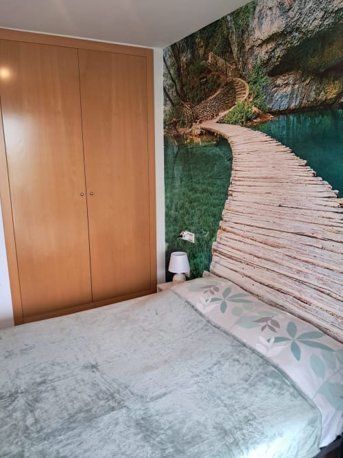 Chambre moderne avec armoire en bois, fresque murale vue montagne et passerelle en bois sur eau turquoise, appartement Sant Jordi.